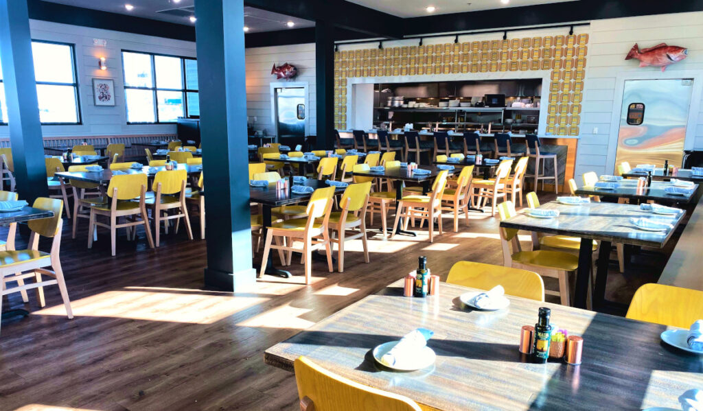 A light-filled restaurant interior with empty tables and yellow chairs