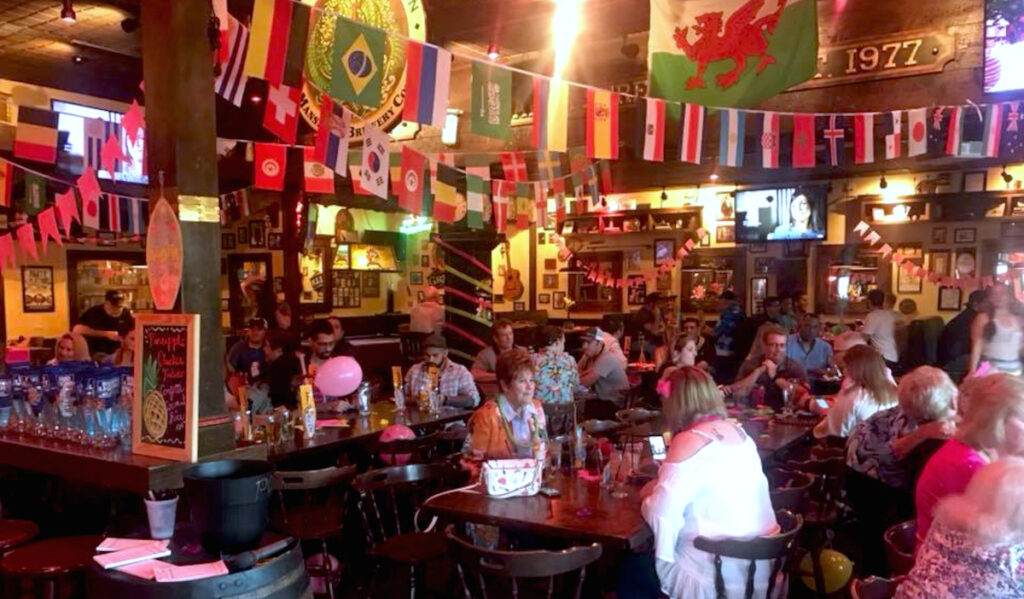 A pub interior with people at tables and banners of country flags strewn across the ceiling