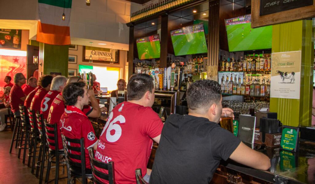 A row of soccer fans in red shirts at a bar watching TV