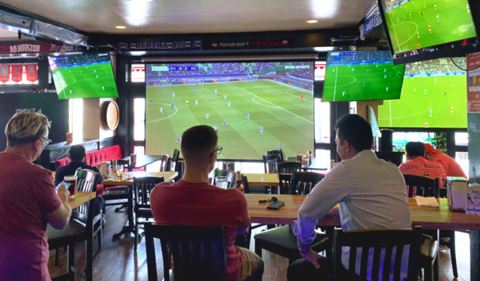 Several people inside a bar watching multiple televisions of soccer