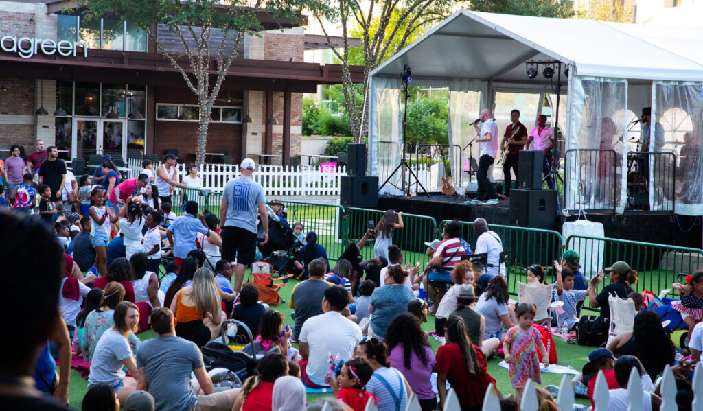 A crowd in lawn chairs and on blankets watch a band perform on a stage