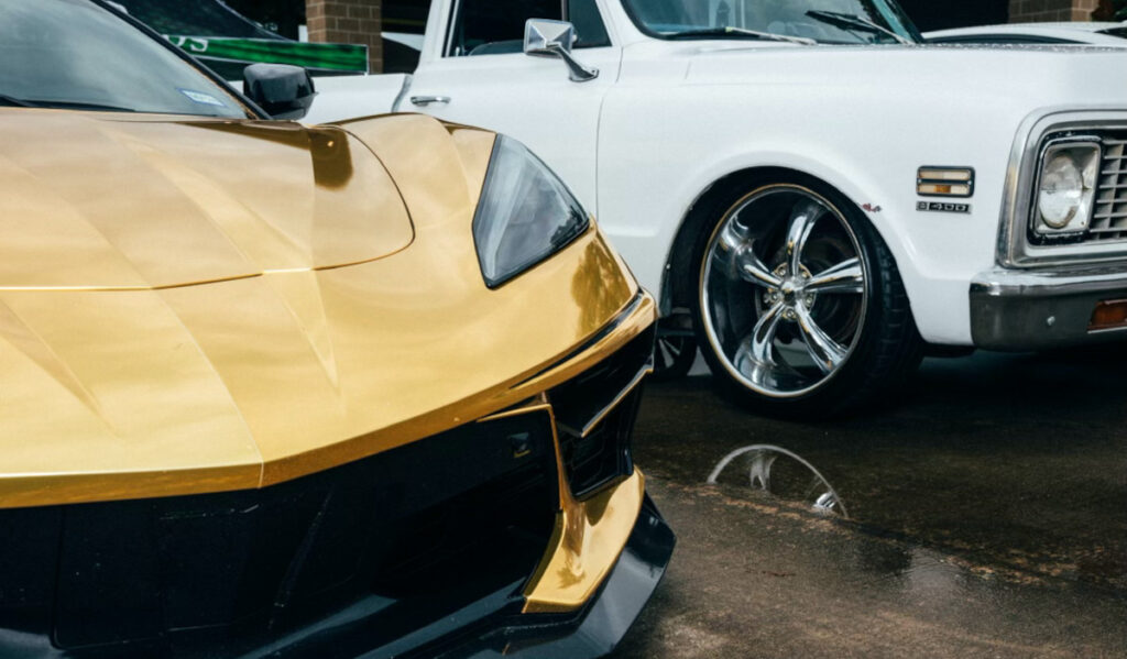 A close-up of a gold Corvette grille next to a white classic pickup