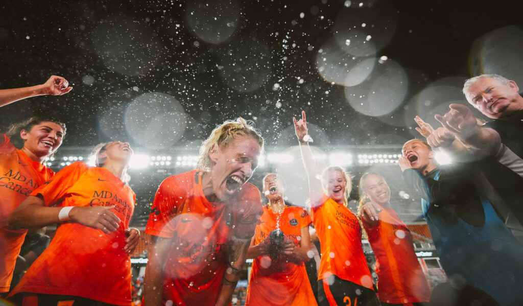 Houston Dash players get doused with water in a huddle