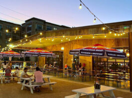 An outdoor bar patio at sunset with people sitting at table under a string of lights