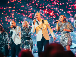 Six members of Rajaton performing on stage in silver formal clothing