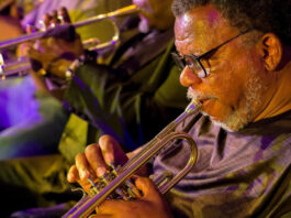 A close up of a man blowing into a trumpet with other trumpeters behind him