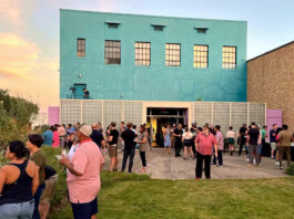 A gathering of people outside of an arts gallery at sunset