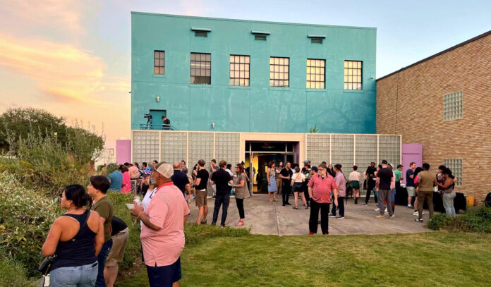 A gathering of people outside of an arts gallery at sunset