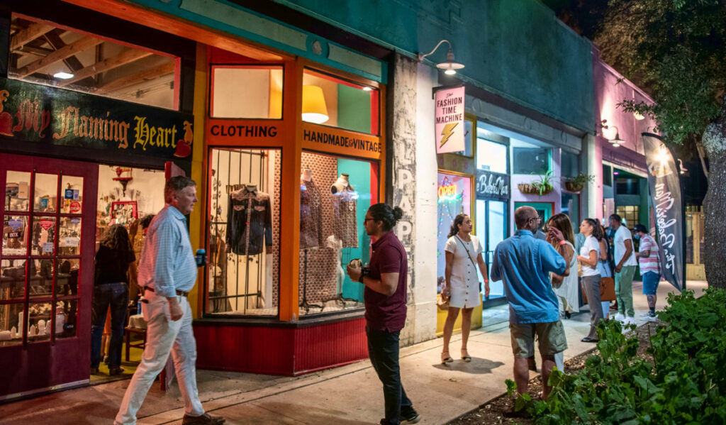 People walking past multiple storefronts at night