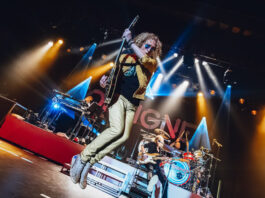 A guitarist jumps in midair while a band plays behind him