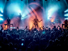 A band performs on stage in silhouette with blue and orange lights behind them