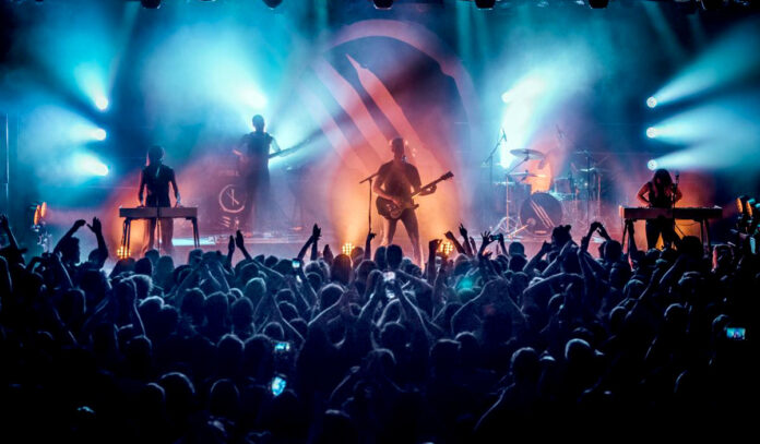 A band performs on stage in silhouette with blue and orange lights behind them