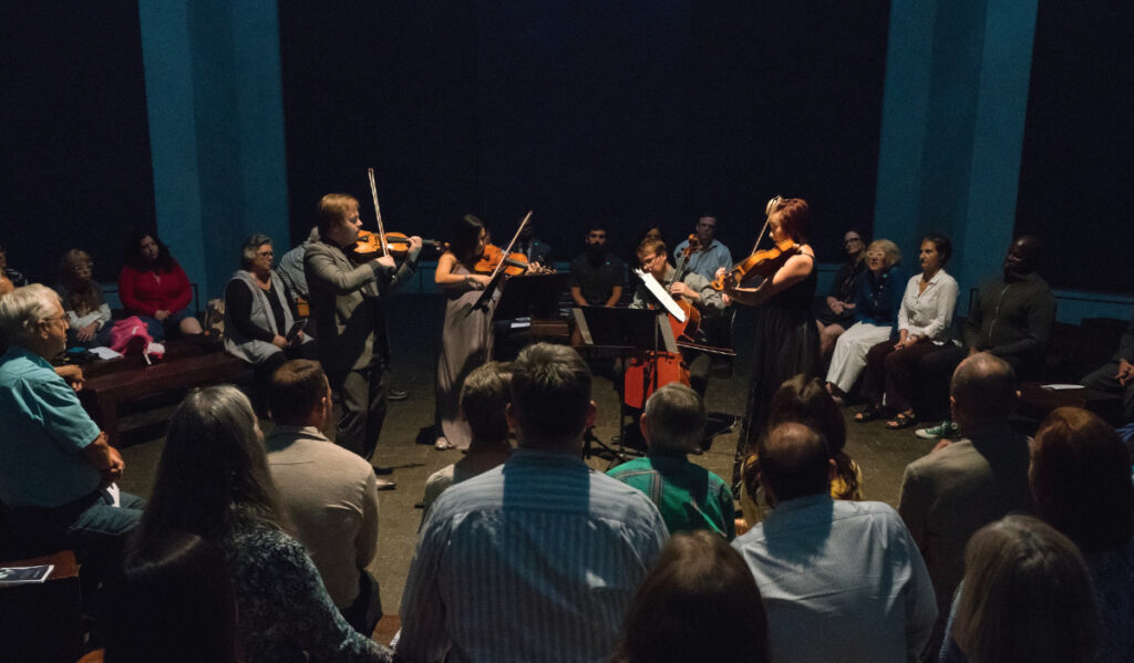 An audience sits in a circle around a quartet performing