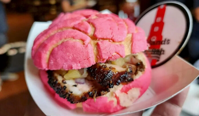 A close up of a barbecue sandwich in a pink concha bread