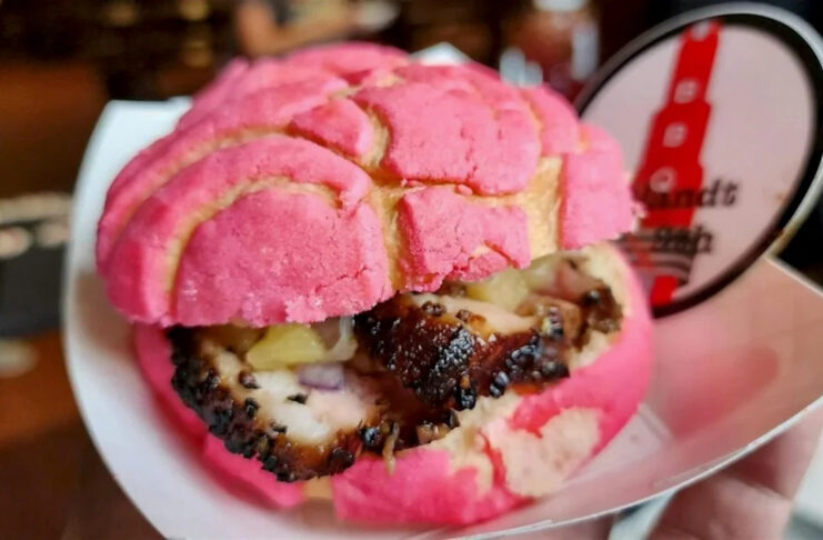 A close up of a barbecue sandwich in a pink concha bread
