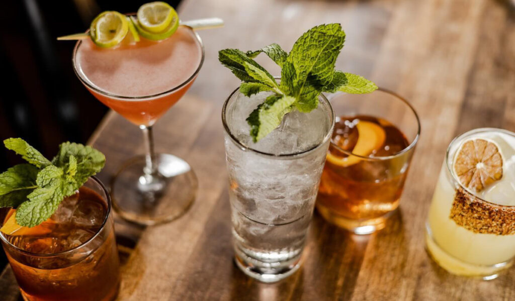 Five cocktails with different garnishes on a table