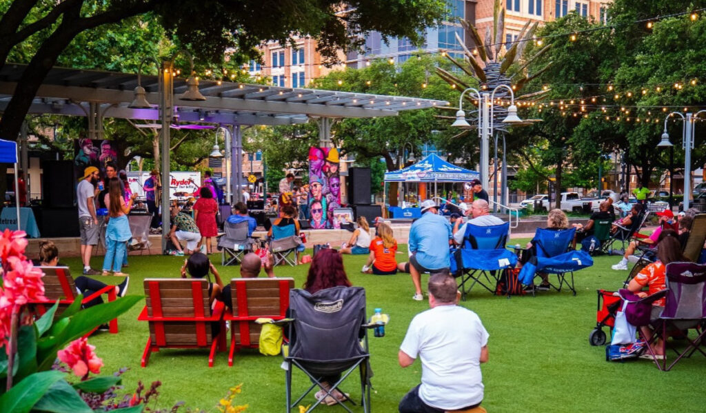 A crowd in lawn chairs and on blankets watching a band perform on a stage in a park