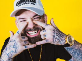 A close up of Paul Wall smiling while holding his hands in an H shape around his mouth