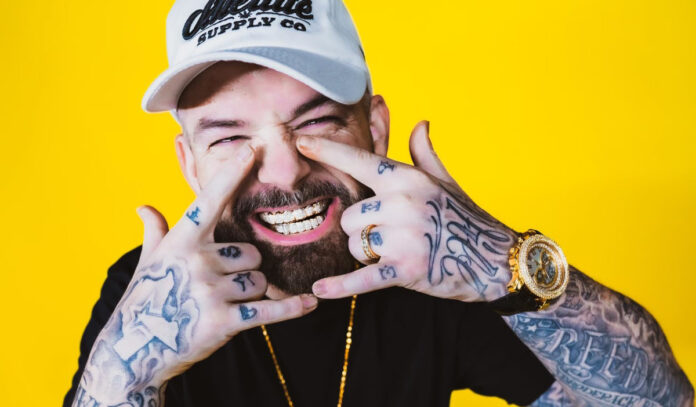 A close up of Paul Wall smiling while holding his hands in an H shape around his mouth