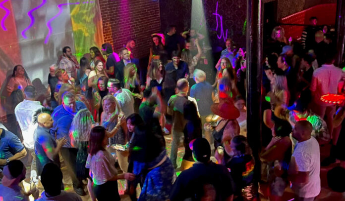 A danceclub crowded with people covered in multi-color lights