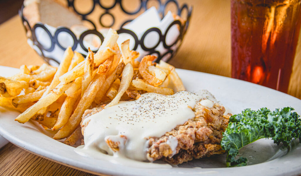 A plate of chicken fried chicken smothers in gravy with fries