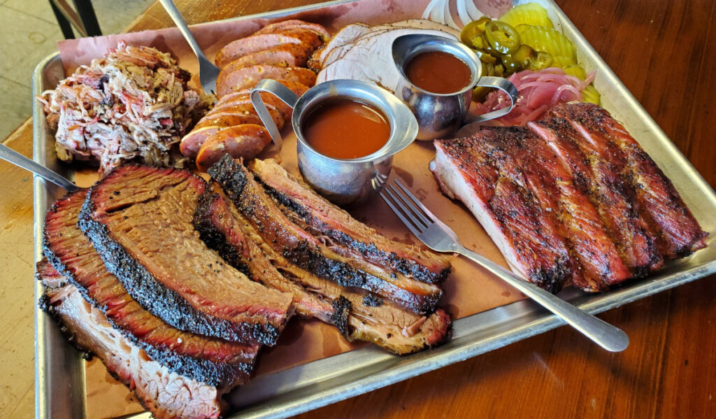 A plate of barbecue brisket, ribs, sausage, and turkey with sides