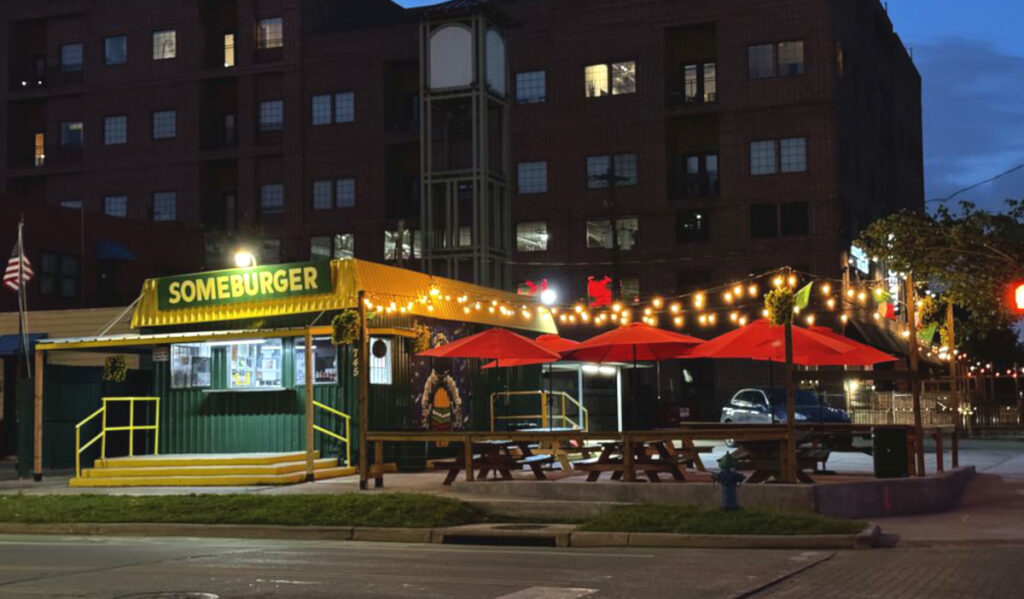 Exterior of Someburger with a patio of red umbrellas lit with string lights at night