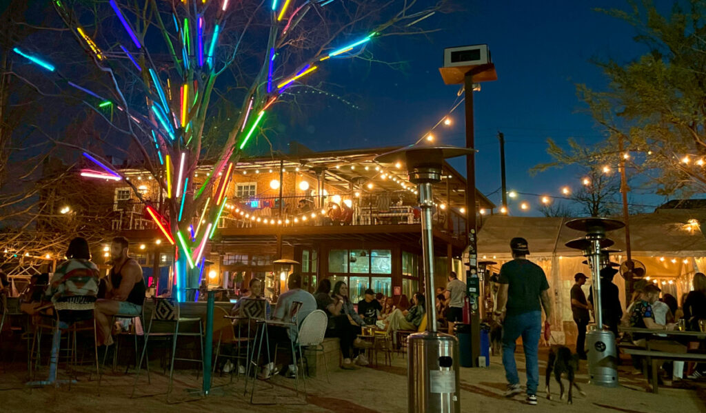 A night scene at a bar's busy outdoor patio with a tree decorated in neon lights
