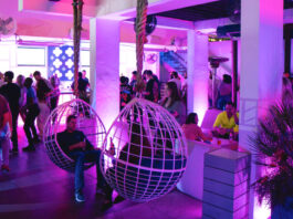 A bar interior lit in purple with two people sitting in suspended swings