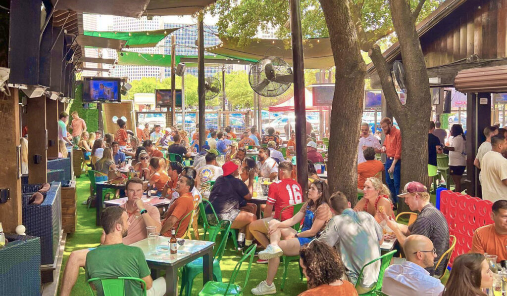 A shady patio filled with people in sports jerseys watching televisions