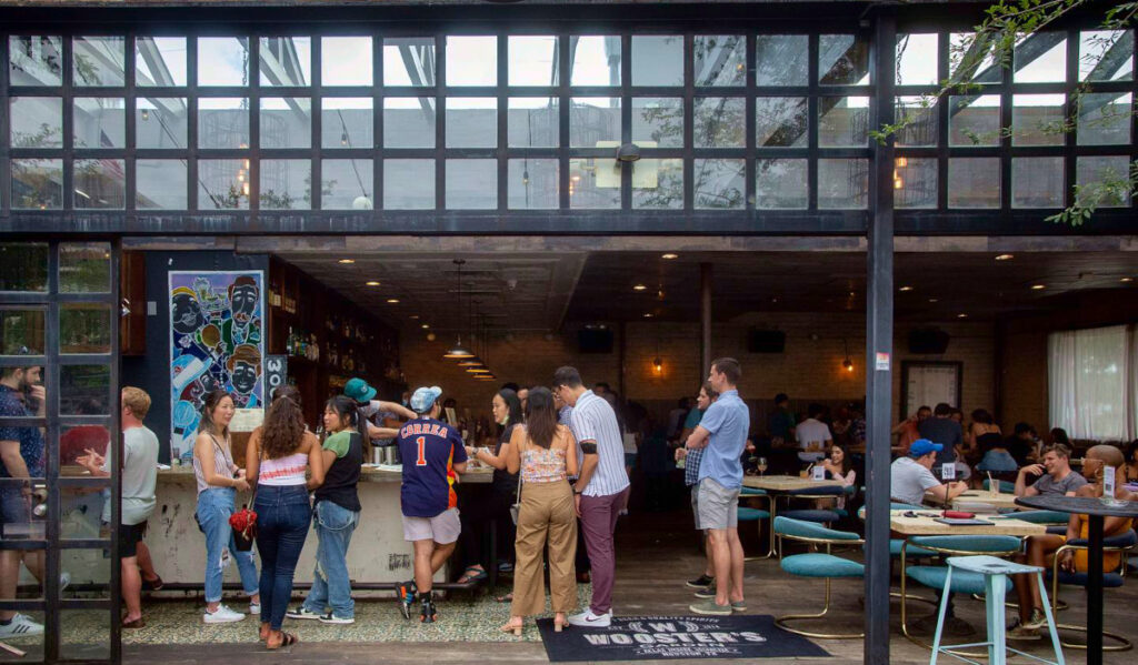 People waiting in line at a bar with an open patio and glass-paneled wall