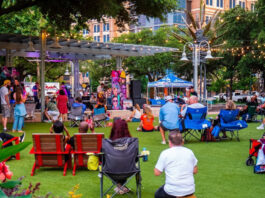 A crowd in lawn chairs and on blankets watching a band perform on a stage in a park