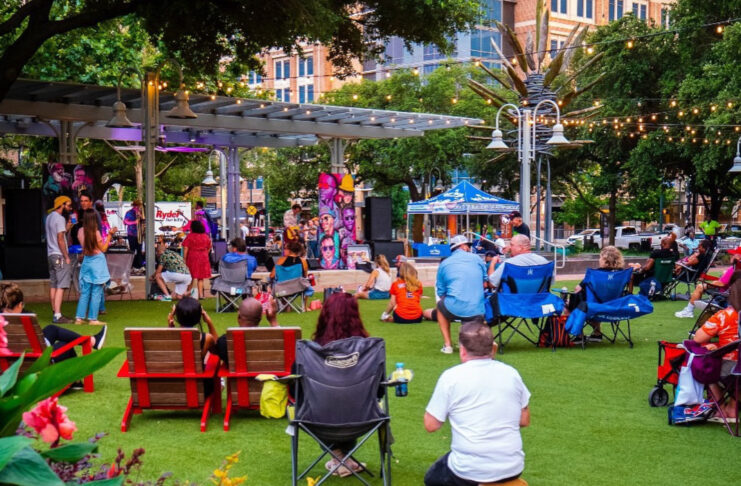 A crowd in lawn chairs and on blankets watching a band perform on a stage in a park