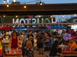 People standing and sitting in an outdoor patio with a "Houston" sign behind them