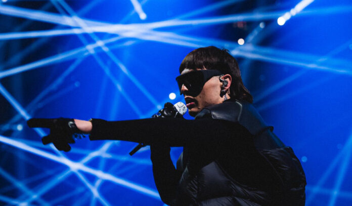 Peso Pluma singing on stage and pointing with a blue laser backdrop