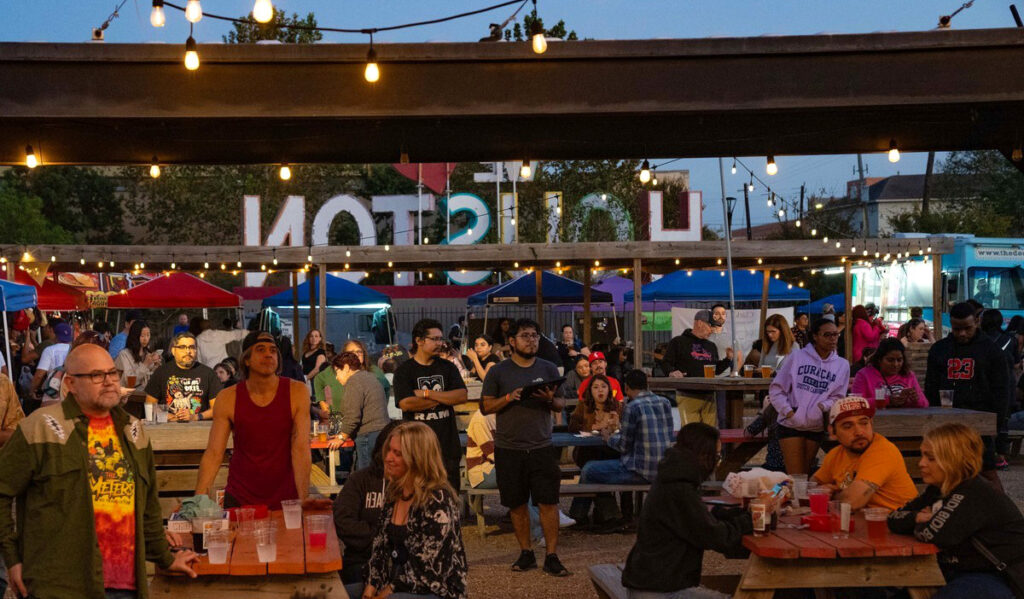 People standing and sitting in an outdoor patio with a "Houston" sign behind them