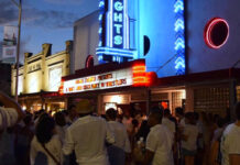 Where to Celebrate White Linen Night in the Heights 2025 A crowd of people in white linens in front of the neon-lit Heights Theater at twilight